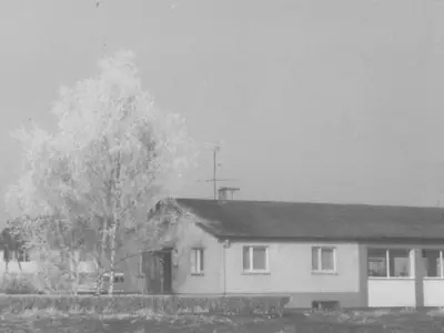 Ein Bild einer Halle mit einem Baum links daneben. Es handelt sich um die ursprünglichen Werkhalle von Huber Maschinenbauteile.